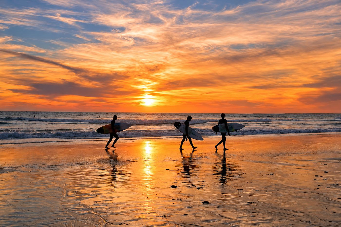 Tres surfistas caminando por la orilla al atardecer
